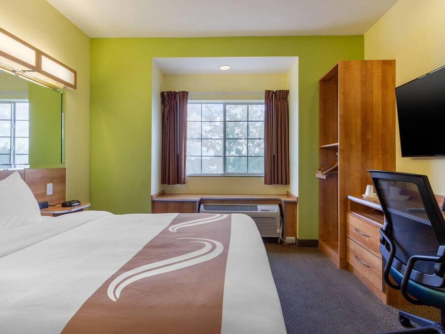 A hotel room with a bed, a desk, a chair, a TV, and a window with curtains.