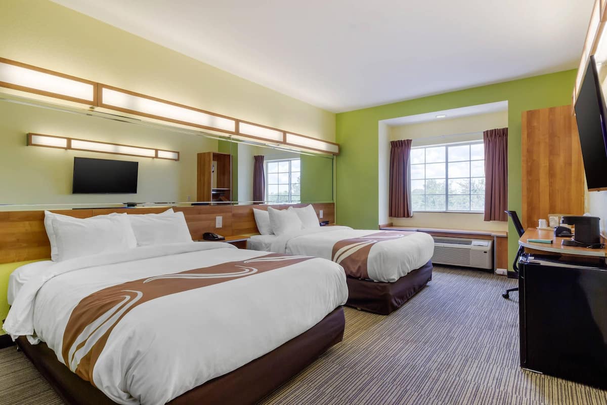 A hotel room with two beds, a desk, a television, and a large window with curtains.