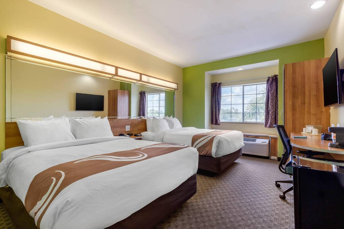 A hotel room with two beds, a desk, a chair, a TV, and a window with curtains.