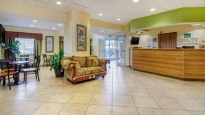 A hotel lobby with a reception desk, a sofa, and a dining area with chairs and tables. - Quality Inn & Suites Lehigh Acres Fort Myers (Lehigh Acres)