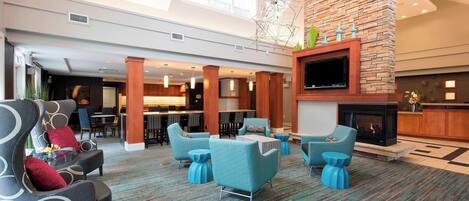 A spacious lobby with a high ceiling, a stone fireplace, and modern seating arrangements.