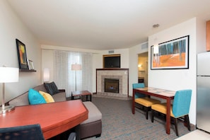 Une chambre d’hôtel comprenant un coin salon, une cheminée, une table à manger avec des chaises, un téléviseur fixé au-dessus de la cheminée et un réfrigérateur.