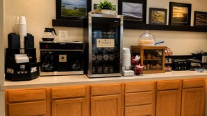 A hotel reception area with a coffee station, a refrigerator, and a display of framed pictures.
