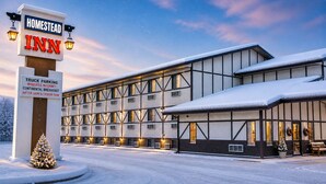 A modern building with a sign for Homestead Inn, featuring amenities like truck parking, wireless internet, continental breakfast, hot tub, sauna, and exercise room.