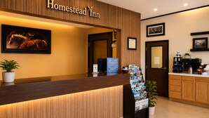 A reception desk with a wooden finish, a framed horse painting, a sign for 'Homestead Inn,' and a coffee station.