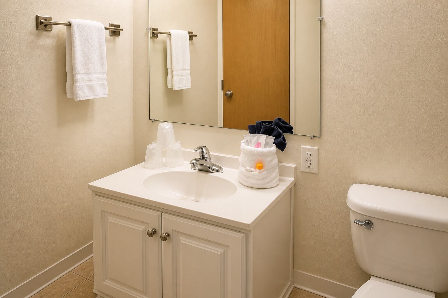 A bathroom with a white sink, a mirror, a toilet, and a towel rack with two towels.