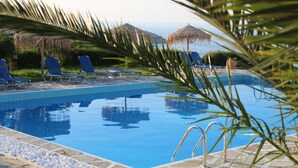 A swimming pool with lounge chairs and a stone border. - Bellevue Village (Malevizi)