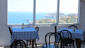 A dining area with checkered tablecloths and metal chairs, overlooking a coastal view. - Bellevue Village (Malevizi)