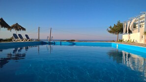 A clear blue swimming pool with lounge chairs and a view of the ocean.