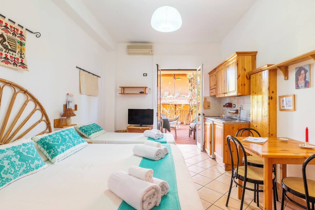 A hotel room with two beds, a dining table, chairs, a TV, and a balcony with a view.