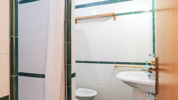 A bathroom with a shower, toilet, sink, and a small stool.