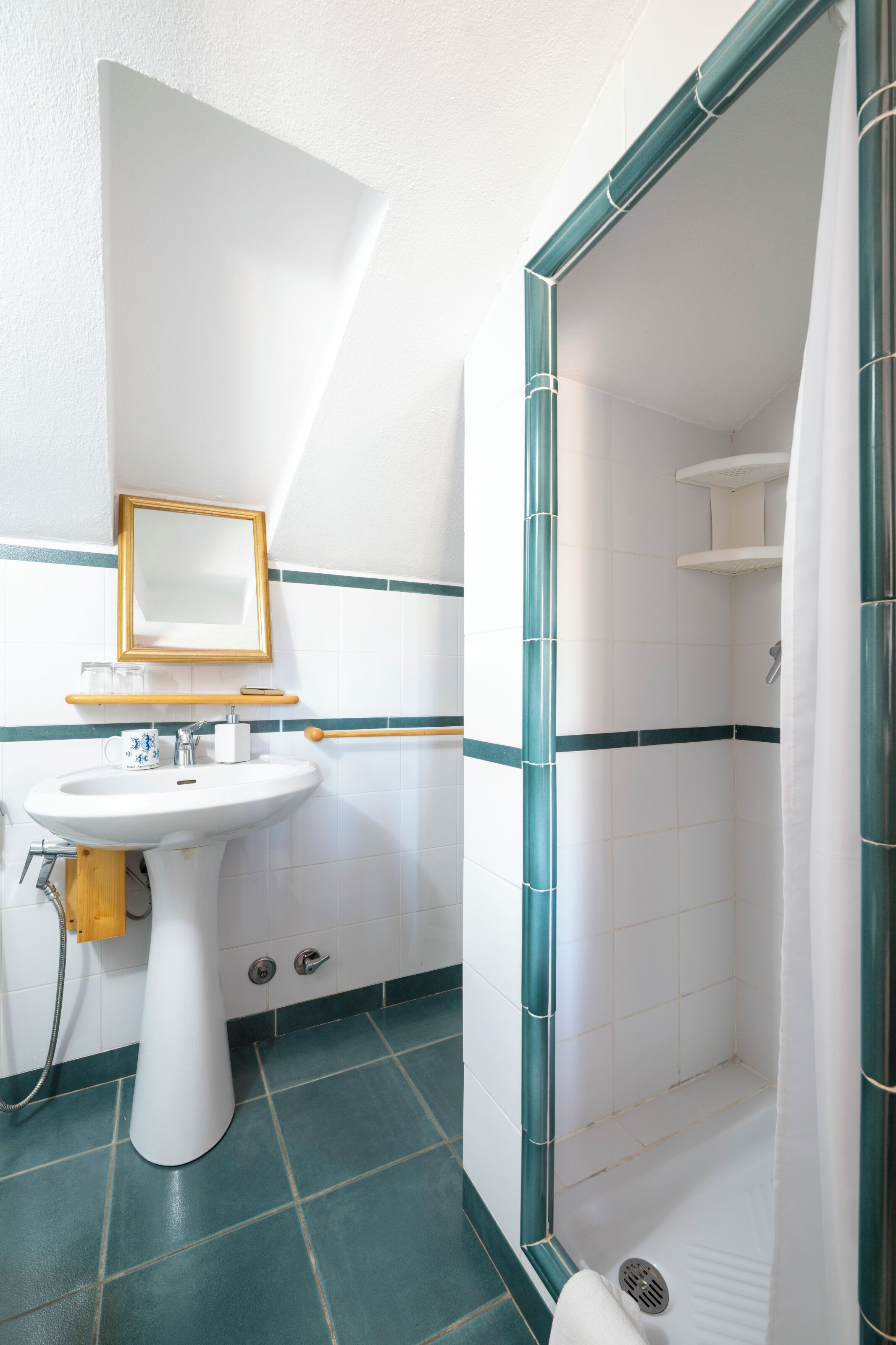 Een badkamer met een wastafel op voet, een spiegel, een douche met gordijn en een betegelde vloer.