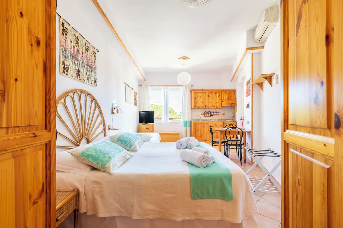 A cozy bedroom with a large bed, wooden headboard, and a view of the kitchen.