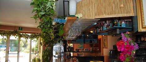 Una zona de bar con una persiana de bambú, copas colgantes y una variedad de botellas y vasos en estantes.
