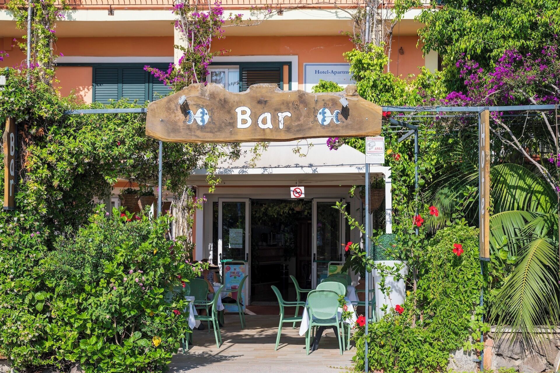 A bar with a wooden sign, outdoor seating, and a building in the background.