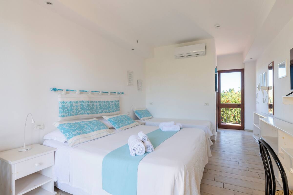 A hotel room with a bed, bedside table, and a view of the outside.