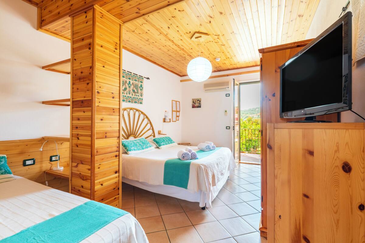 A wooden-paneled room with a bed, a television, and a view of greenery outside.