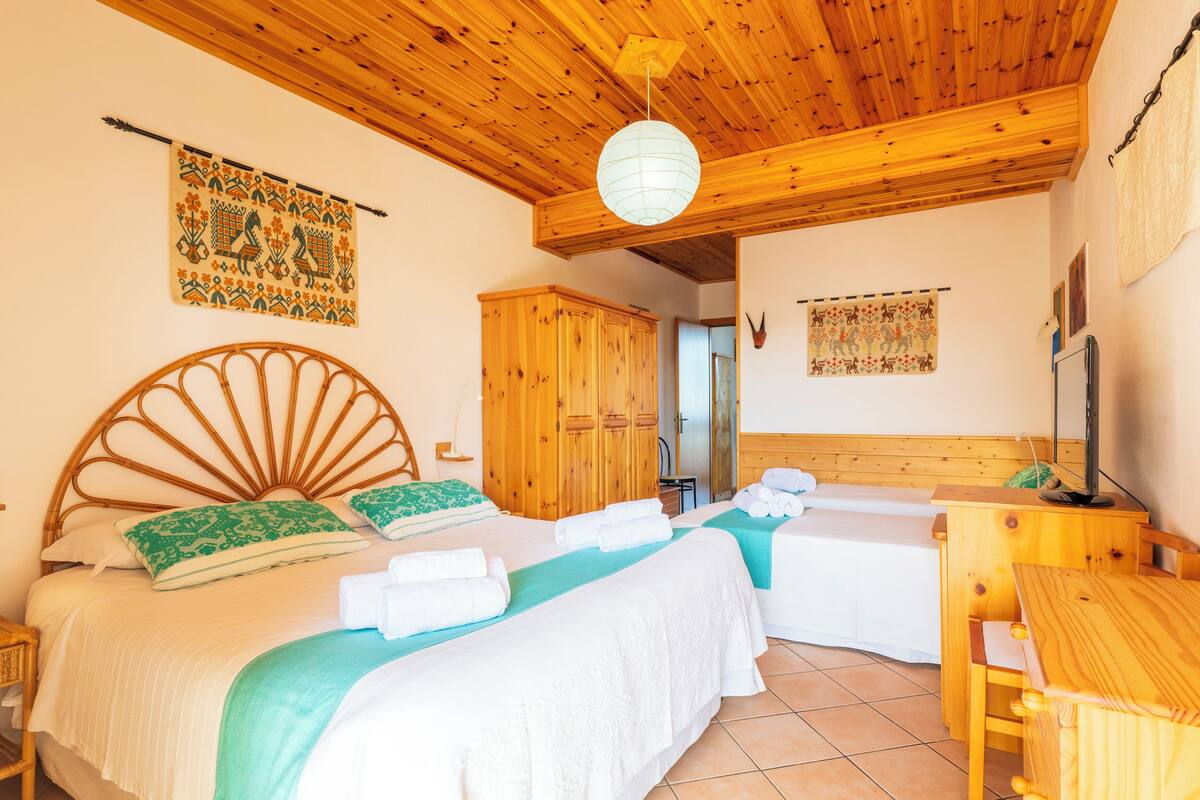 A room with two beds, wooden headboards, a wooden wardrobe, a wooden table, and a hanging light fixture.