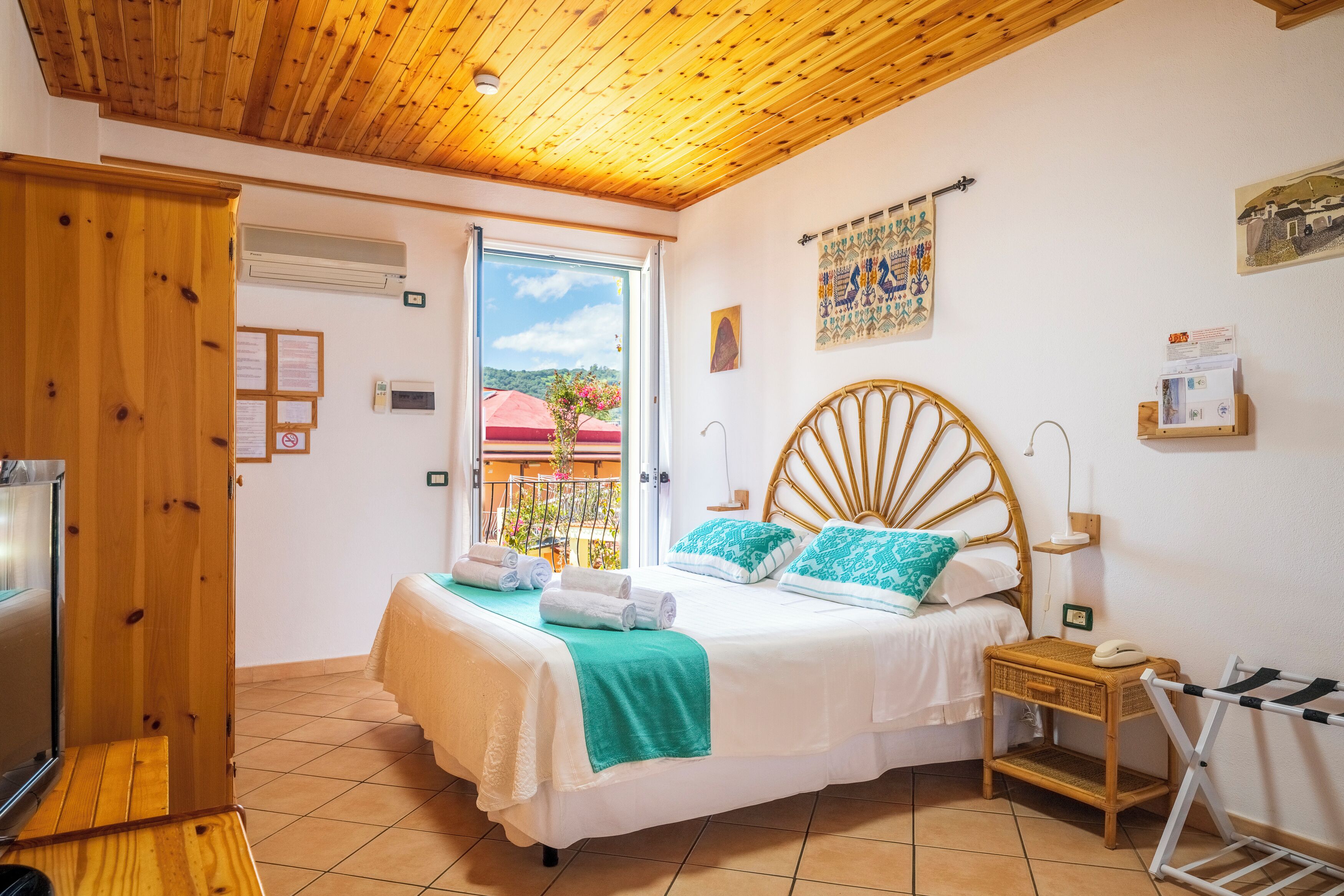 Un dormitorio con cama, techo de madera, ventana con vistas, mesita de noche y estante fijado a la pared.