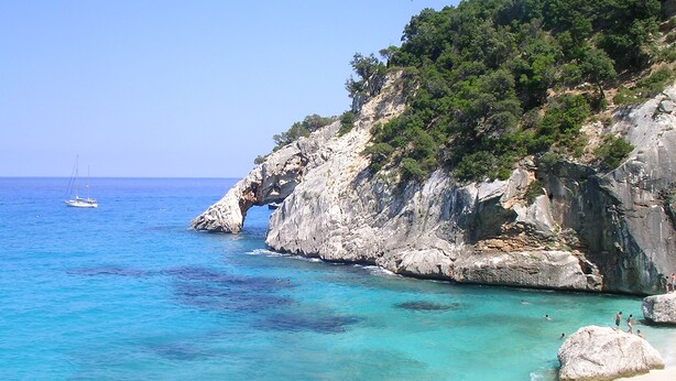 A coastal landscape with clear turquoise waters, rocky cliffs, and a small boat in the distance. - Aparthotel Domus De Janas Sul Mare (Bari Sardo)