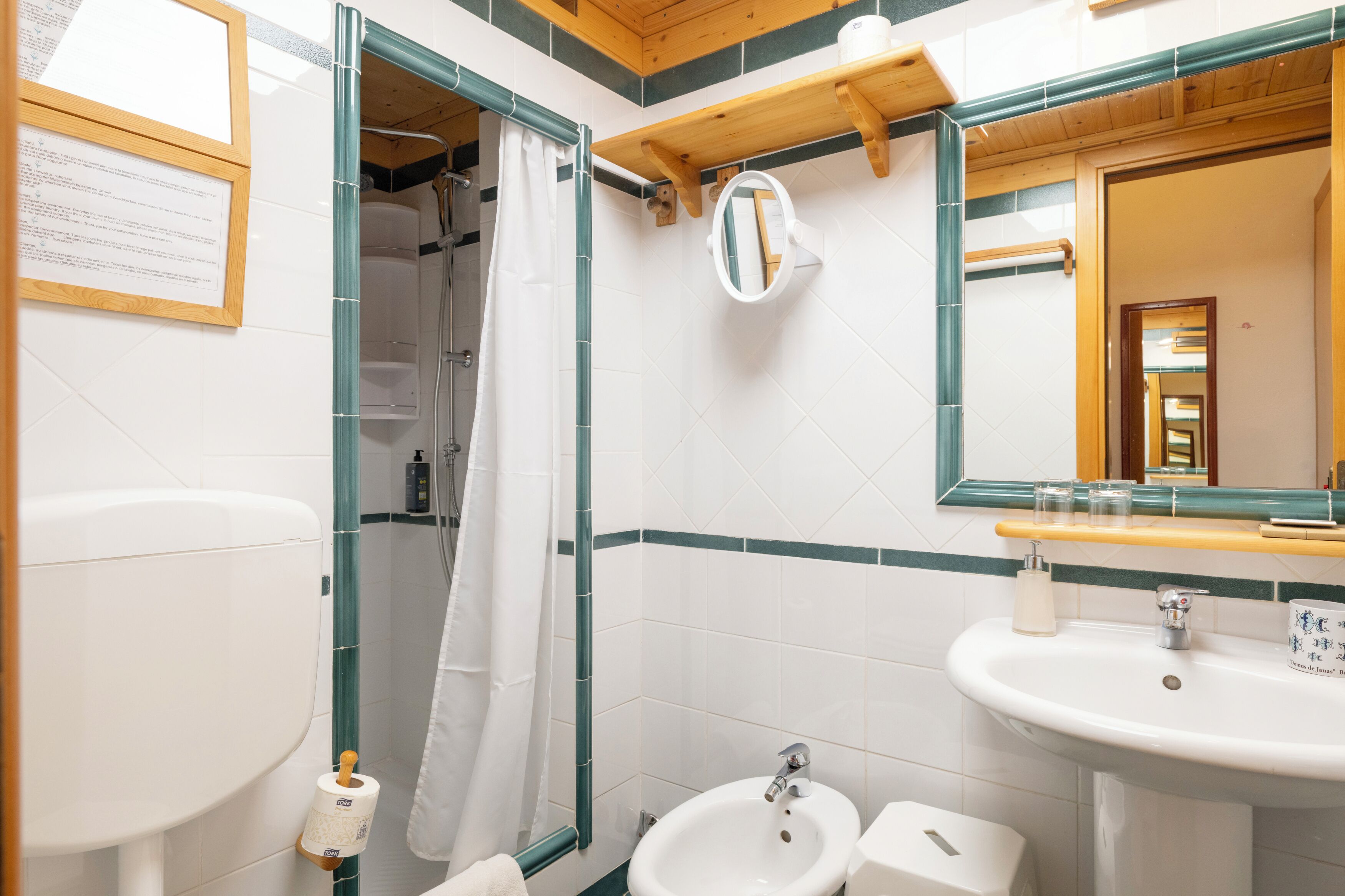 A bathroom with a toilet, bidet, sink, mirror, and shower curtain.