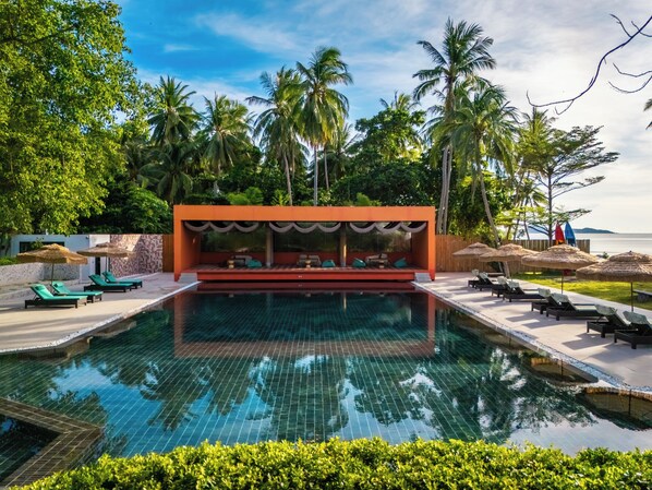 A pool area with lounge chairs and a covered seating area, surrounded by palm trees and a view of the sea. - Tolani Resort Koh Samui (Koh Samui)