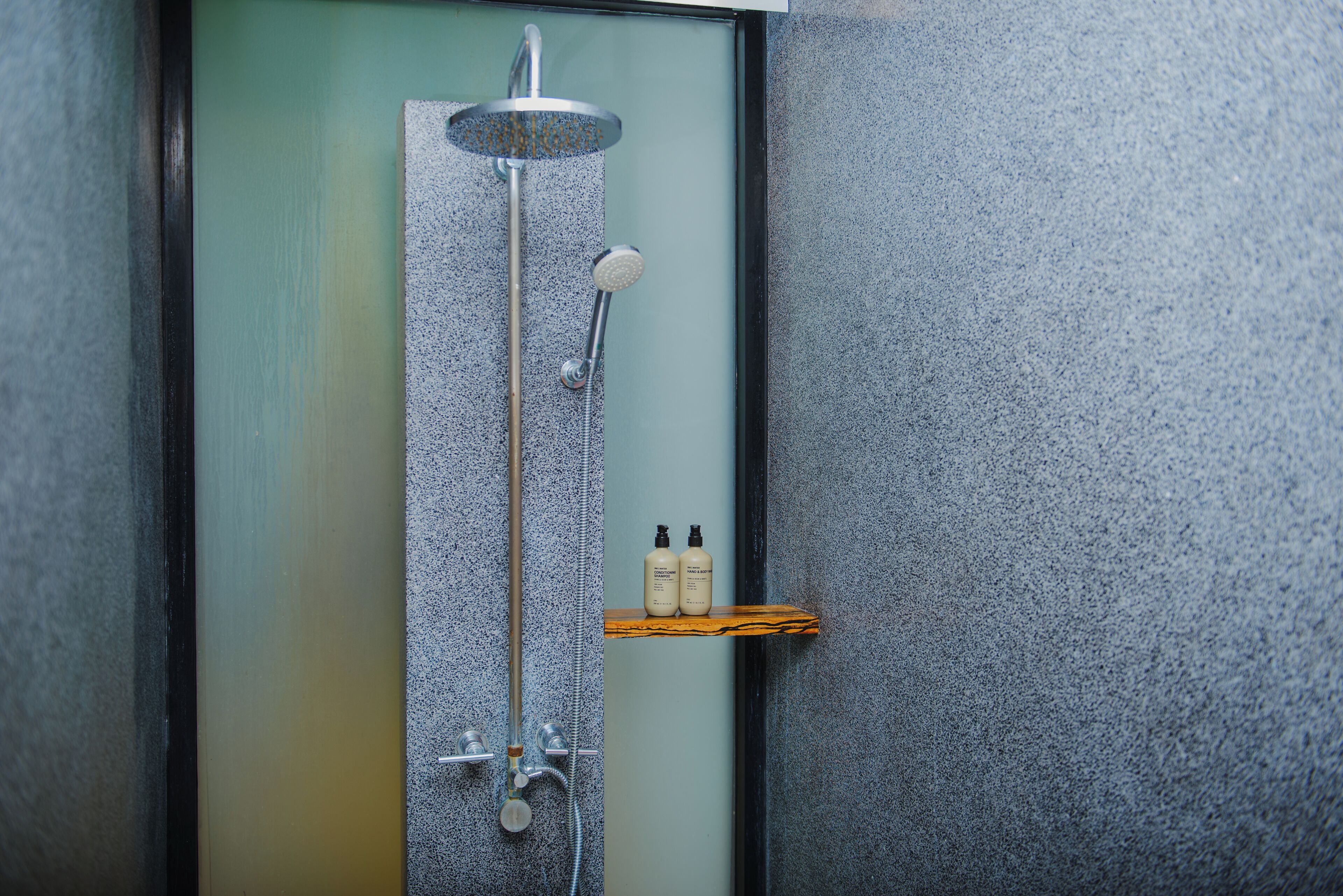 A shower with a rain showerhead, a handheld showerhead, and a handheld massager. There is a shelf with two bottles of shampoo and conditioner.