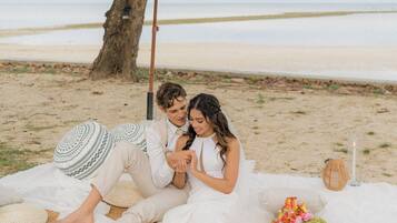 Escena de playa con una sombrilla de paja, una manta y un ramo de flores.