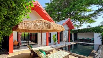 A poolside area with lounge chairs, a thatched umbrella, and a pool.