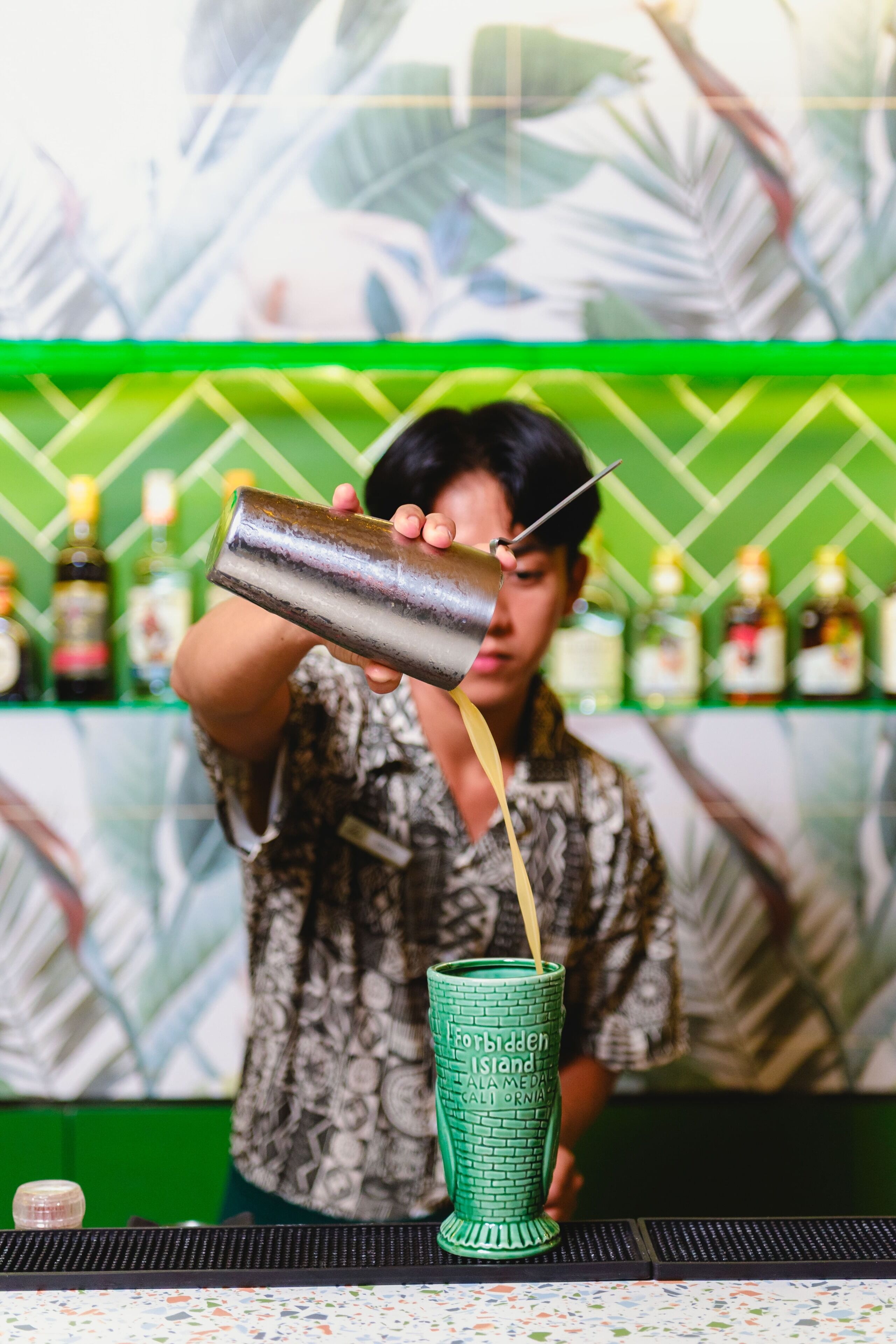 Un cantinero sirviendo una bebida en un vaso verde con diseño de ladrillos.