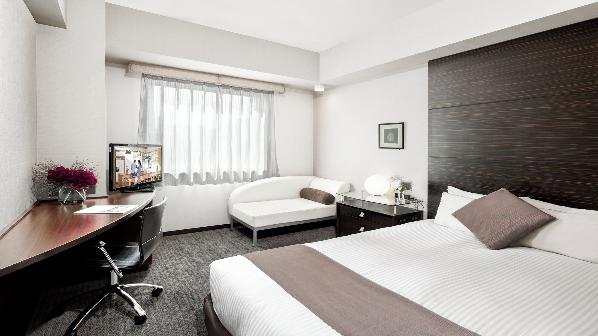 A hotel room with a bed, a desk, a chair, a TV, and a window with curtains.