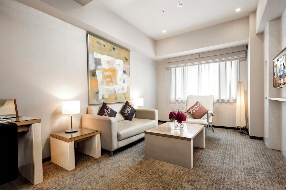 A modern hotel room with a sofa, a coffee table, a desk, and a large abstract painting.
