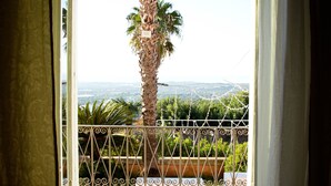A view from a balcony with a metal railing, a palm tree, and a distant landscape. - Villa Principe di Belmonte (Ispica)