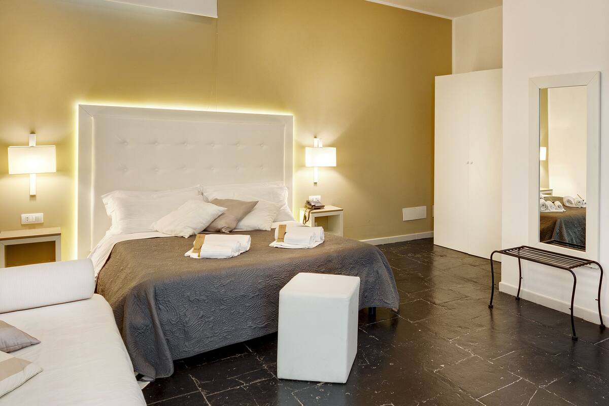 A hotel room with a large bed, bedside lamps, a wardrobe, and a mirror.