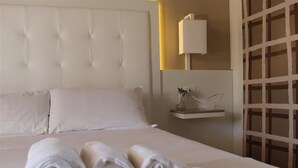 A neatly made bed with rolled towels, a tufted headboard, a bedside table with a lamp, and a decorative wall piece. - Villa Principe di Belmonte (Ispica)