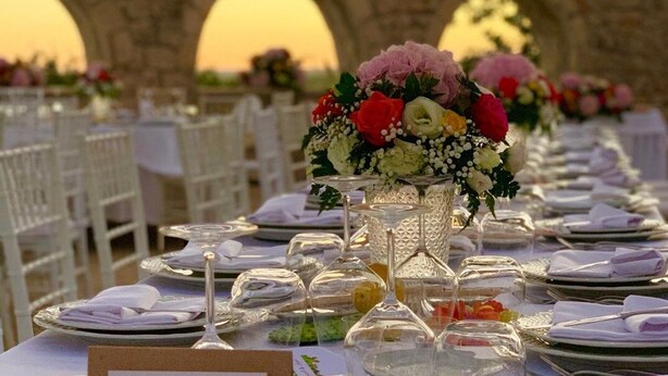 A long table set for a formal event with glassware and floral centerpieces, set against a stone archway backdrop. - Villa Principe di Belmonte (Ispica)