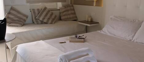 A hotel room with two beds, a bedside table with a lamp, and a small table with a book and glasses.