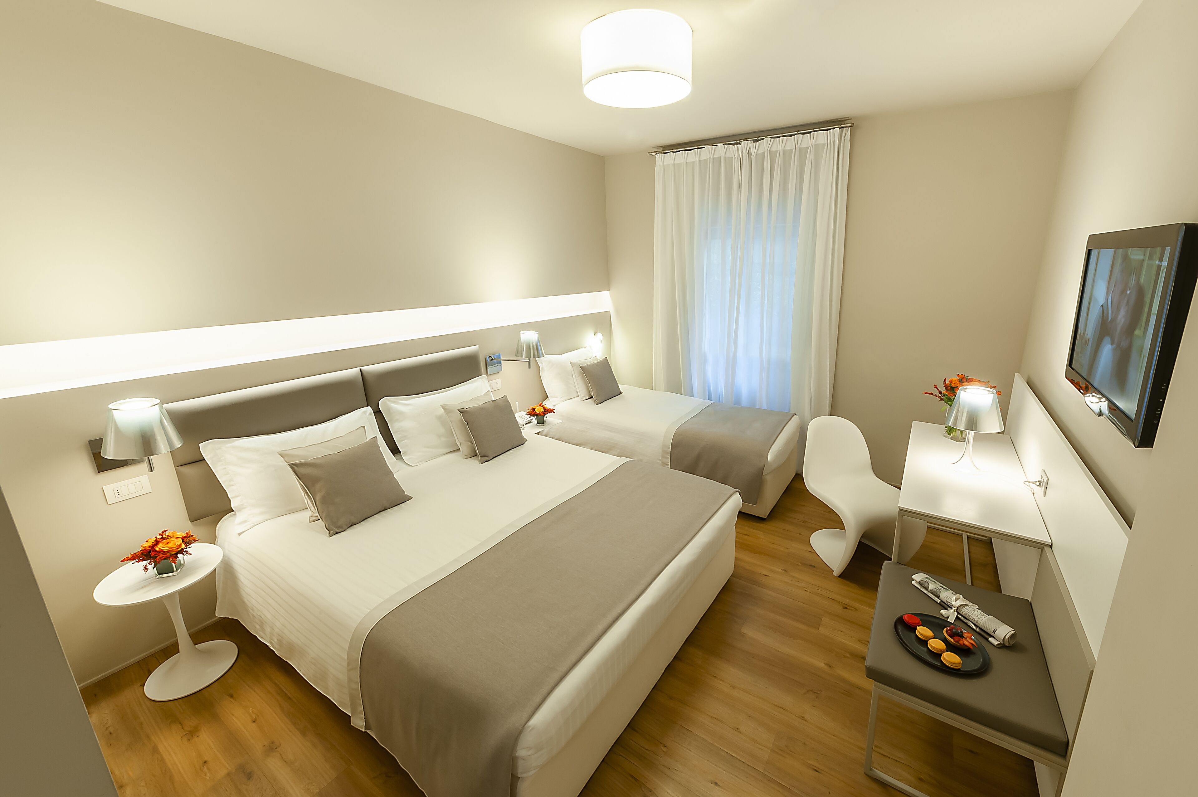Quarto de hotel moderno com duas camas, uma escrivaninha, uma cadeira e uma mesinha com controle remoto e lanches.