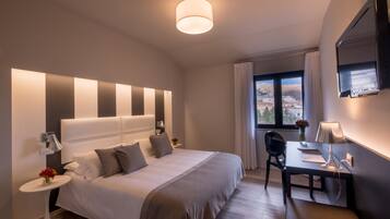 Quarto de hotel moderno com uma cama grande, mesas de cabeceira, escrivaninha e televisão.
