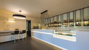 A modern bar area with a long counter, bar stools, and a glass display case. - Hotel Monte Meraviglia (Cascia)