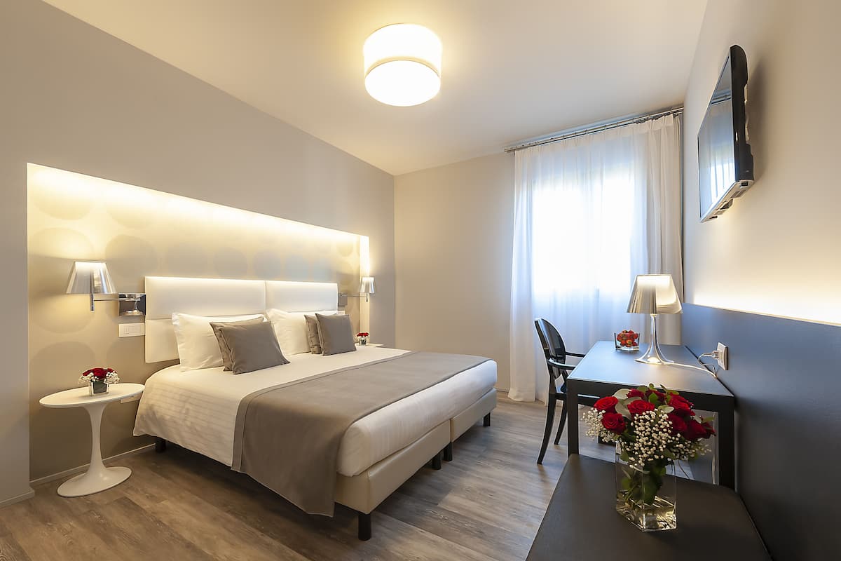 Ein modernes Hotelzimmer mit einem großen Bett, Nachttischen, einem Schreibtisch und einem Flachbildfernseher.