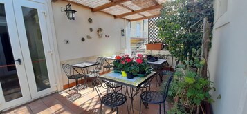 An outdoor patio with a table and chairs, surrounded by potted plants and decorative items.