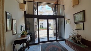 Um saguão de hotel com entrada por porta de vidro, obras de arte emolduradas nas paredes e um banco com arranjo floral.