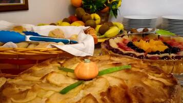A buffet table with various dishes, including a large pie with apple slices and a fruit arrangement.