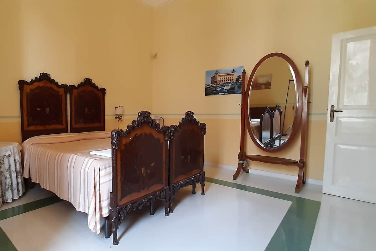 A bedroom with a bed, a bedside table, a mirror, a radiator, and a door.