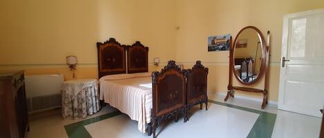 Um quarto com cama, mesa de cabeceira, espelho, radiador e porta.