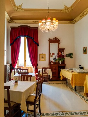 A dining area with a chandelier, red curtains, a wooden cabinet, and a table set for a meal. - Piccolo Hotel Casa Mia (Syracuse)