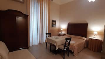 Ein Hotelzimmer mit einem Bett, einem kleinen Tisch mit Stuhl, einem Schreibtisch ebenfalls mit Stuhl, einem Kleiderschrank und zwei Nachttischen mit Lampen.