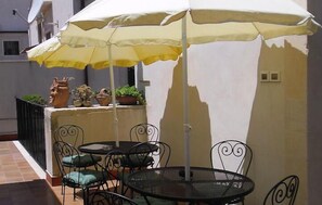 An outdoor patio with a table and chairs under a yellow umbrella, surrounded by potted plants and a white wall. - Piccolo Hotel Casa Mia (Syracuse)