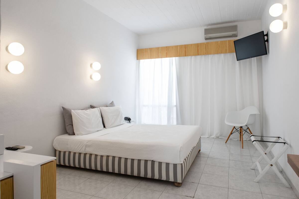 Une chambre d’hôtel moderne équipée d’un lit, d’un bureau, d’une chaise et d’un téléviseur fixé au mur.